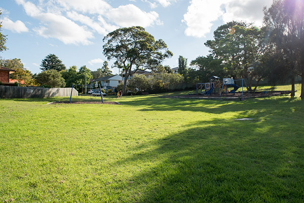 Open space grassed area with shady trees and playground