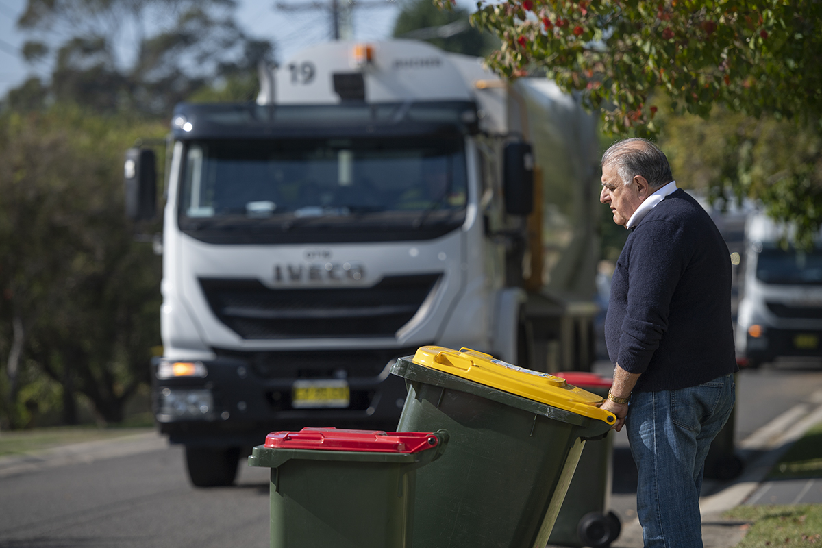 Man putting waste bins on kerb, waste truck in background