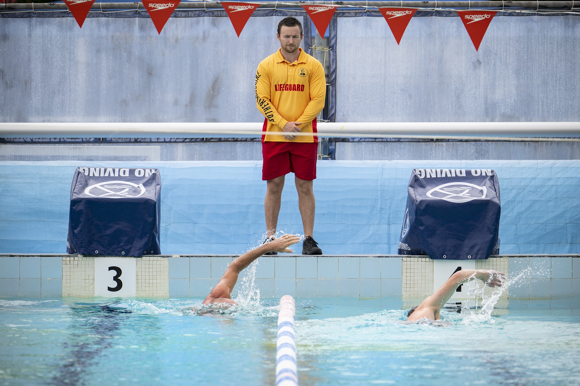 Lifeguard on duty at swimming pool with two swimmers