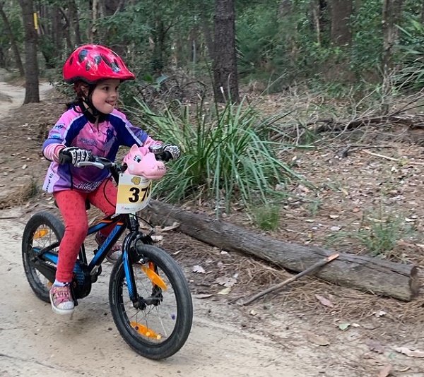 Child on bike, wearing helmet, riding along bush track