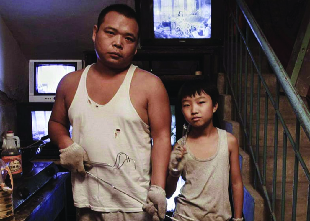 A Chinese man and his son wearing grubby white singlets looking glum.