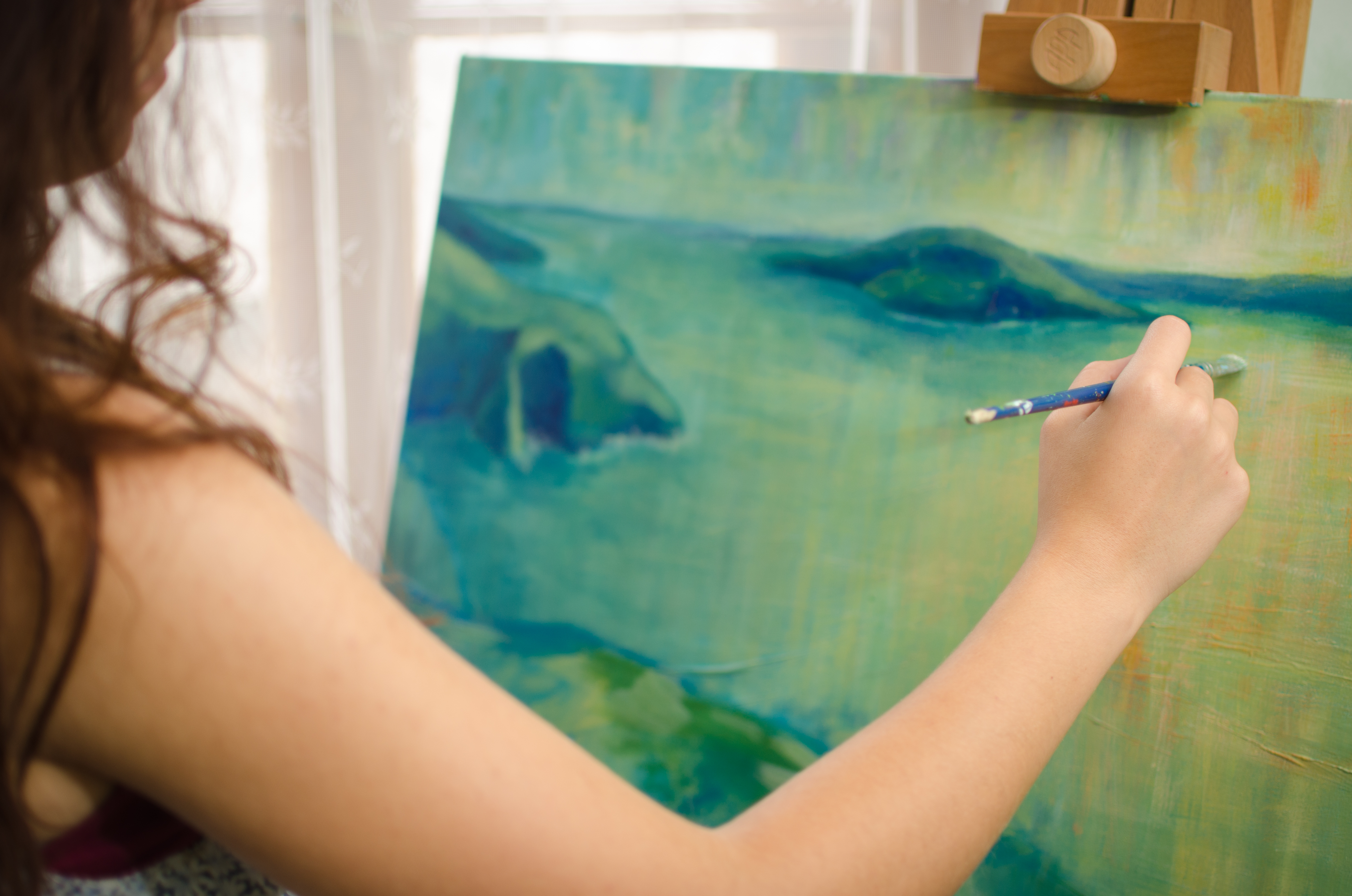 Woman painting coastal landscape in blues and greens.