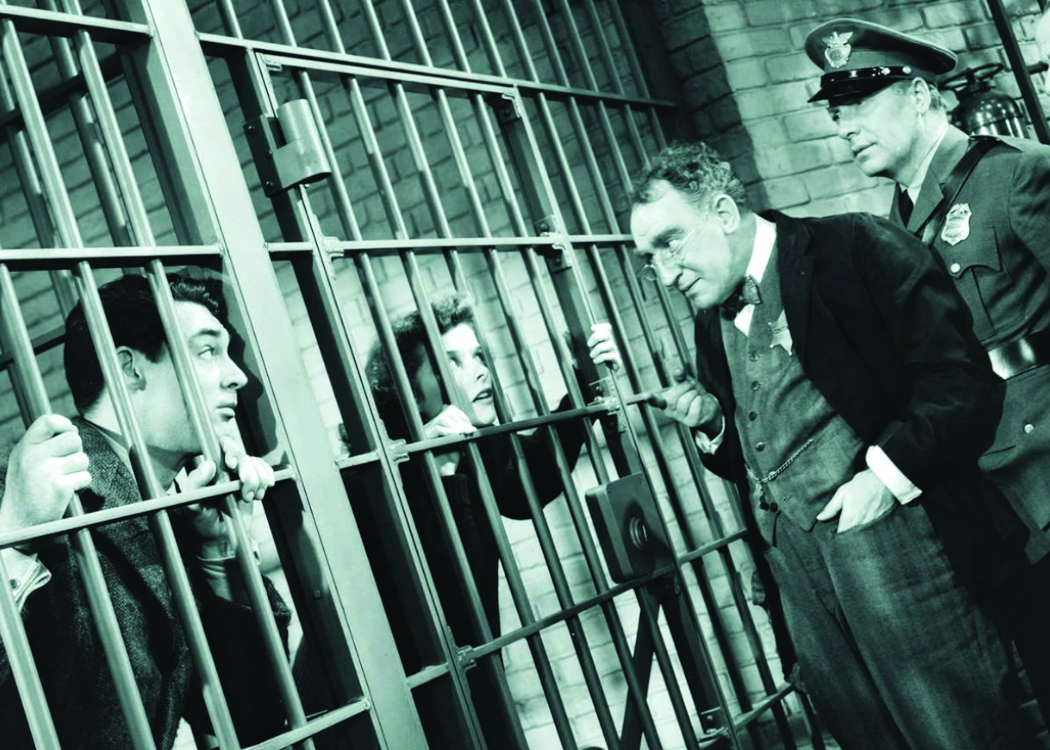 A black and white still of Carey Grant and Katherine Hepburn in a jail cell.