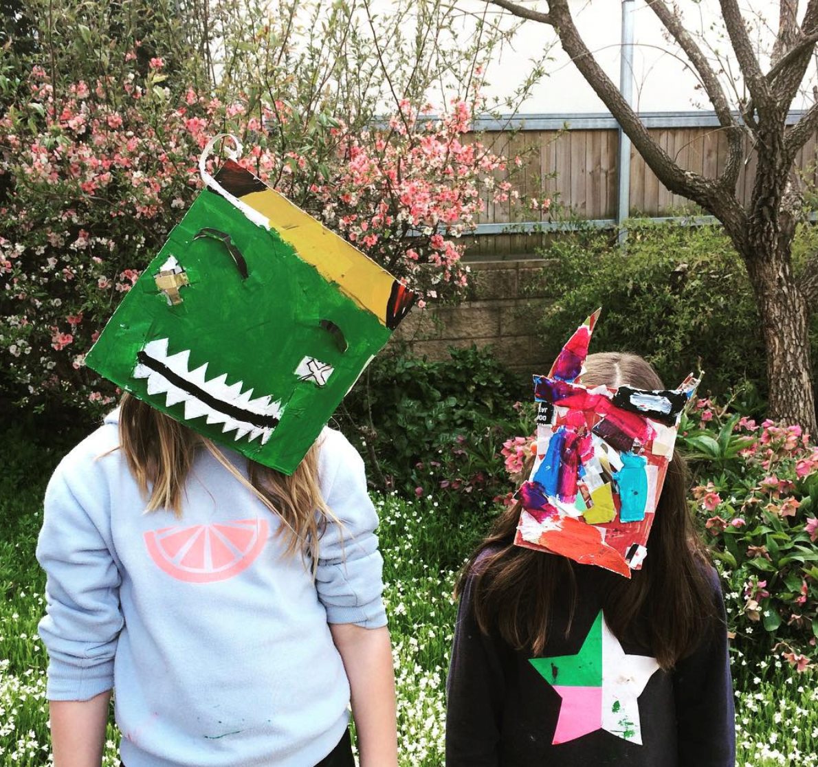 Two people standing outside wearing handmade paper masks.