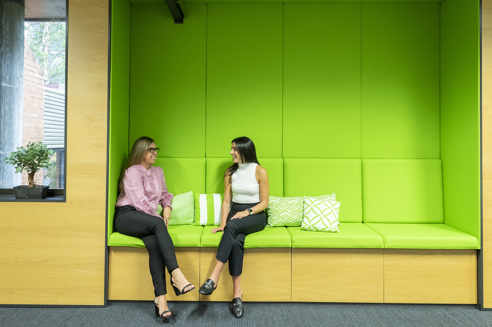 Two colleagues sitting on green chair chatting