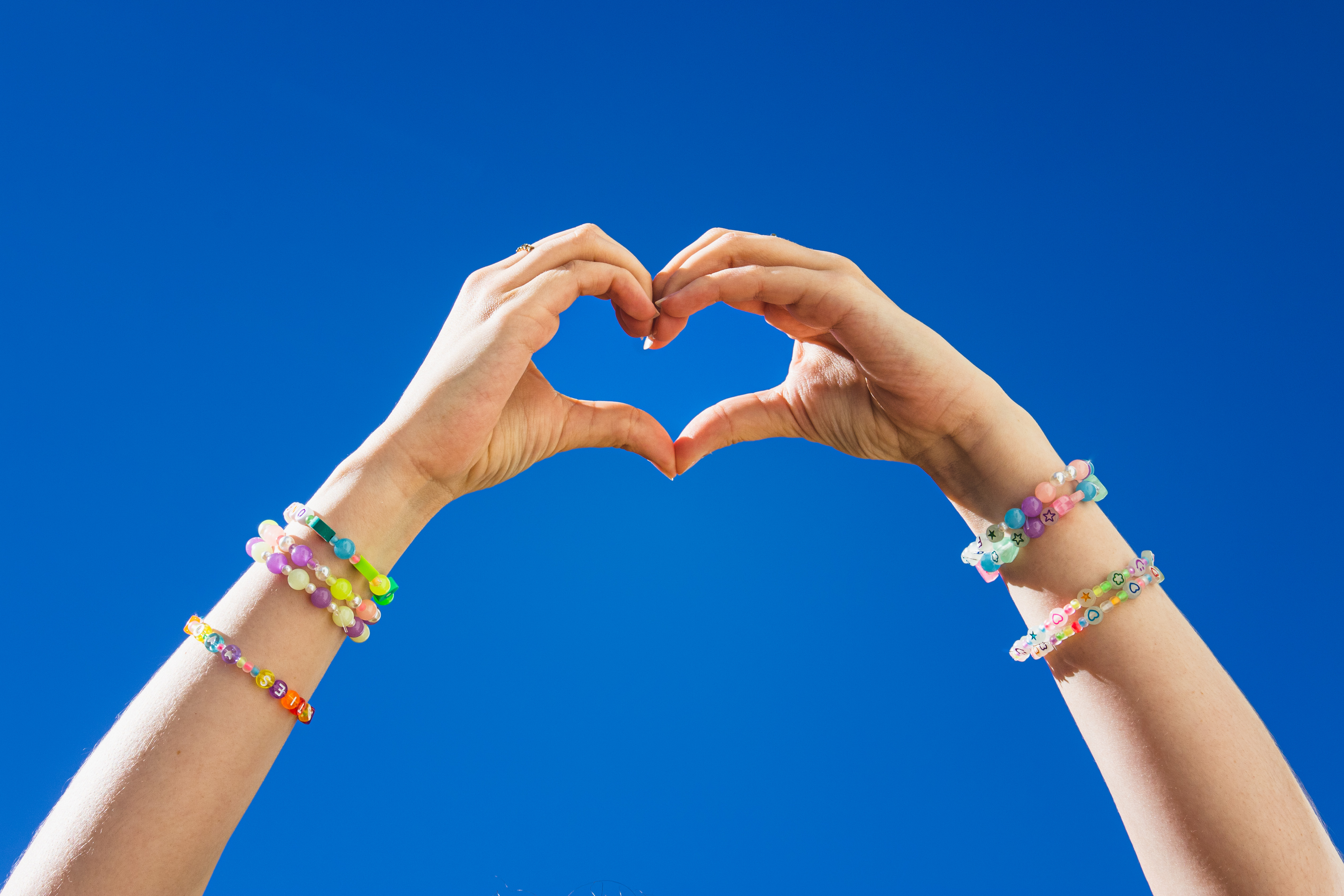 Pair of hands forming a love heart with friendship bracelets