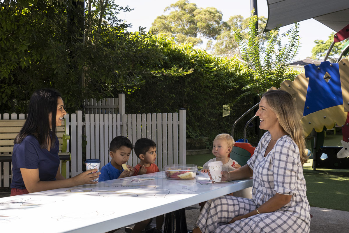 Women chatting and drinking from cups at a playground