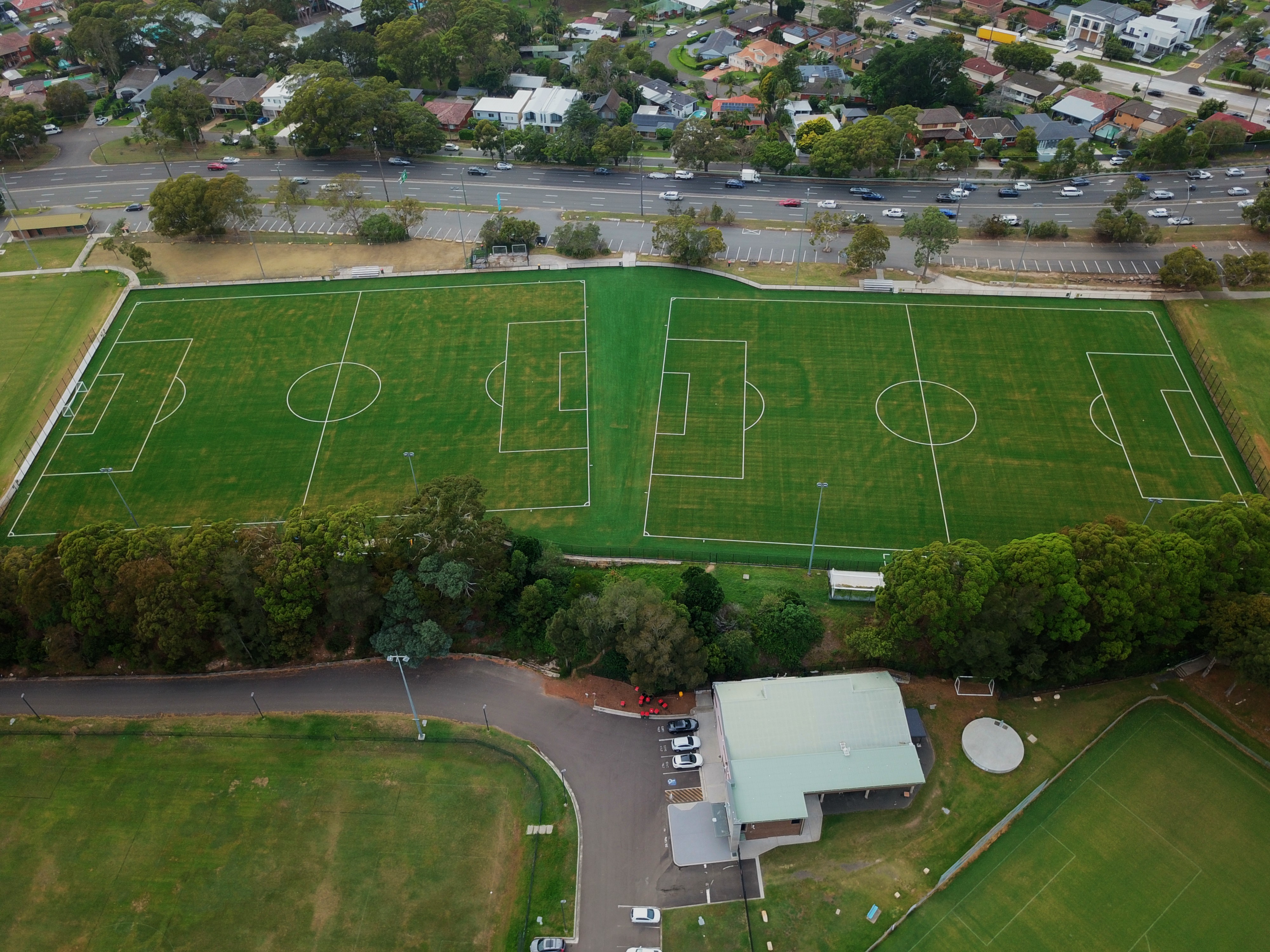 Aerial view of two green synthetic football fields end to end surrounded by trees and road
