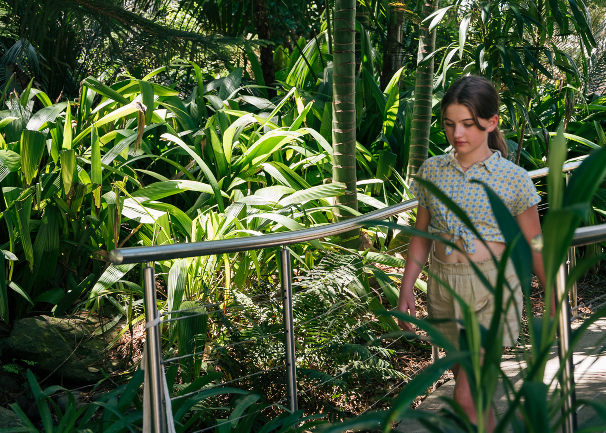 Primary school aged girl walking through tropical garden, the path is defined by a stainless steel railing.