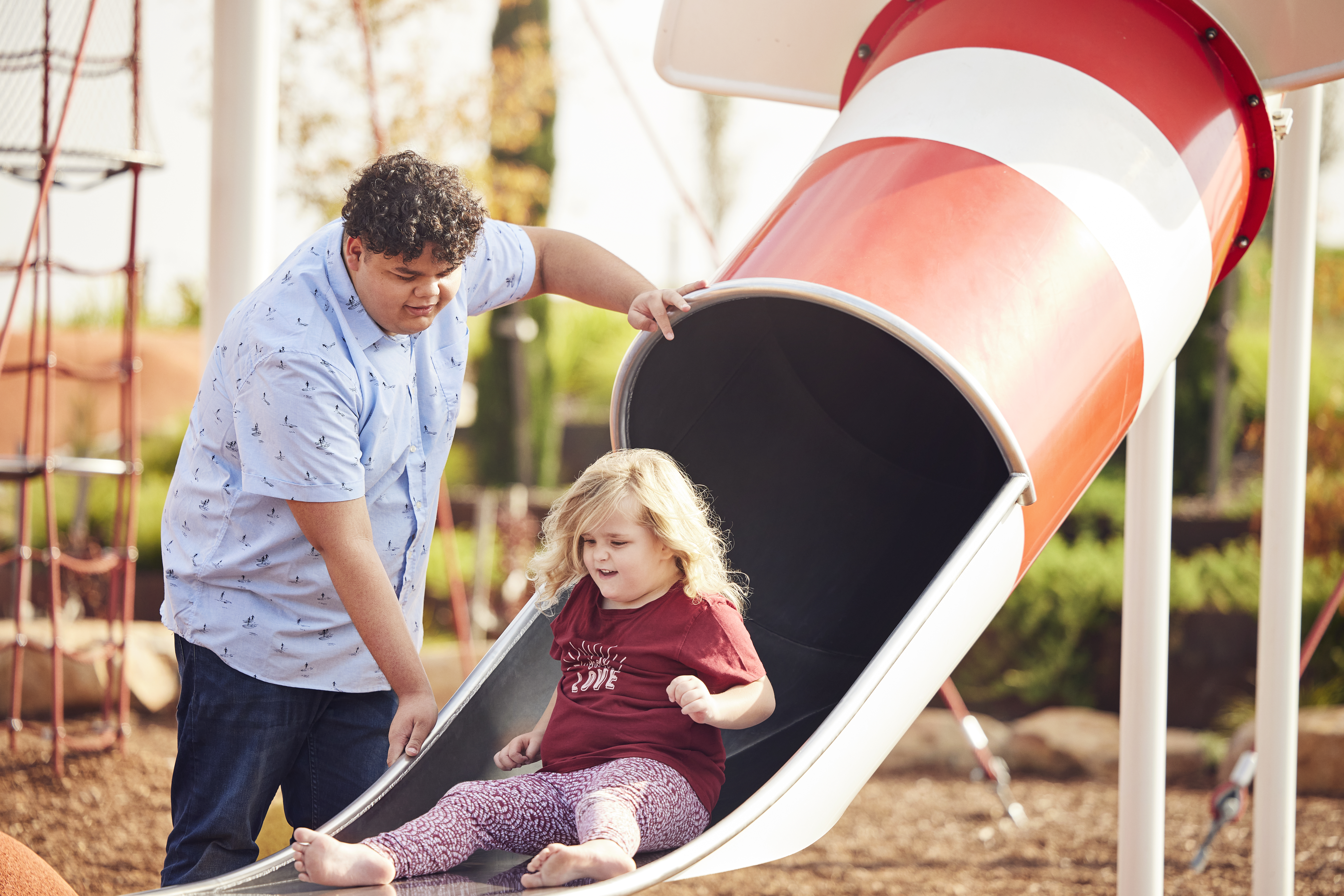 Carer assisting a child down a slide at a playground