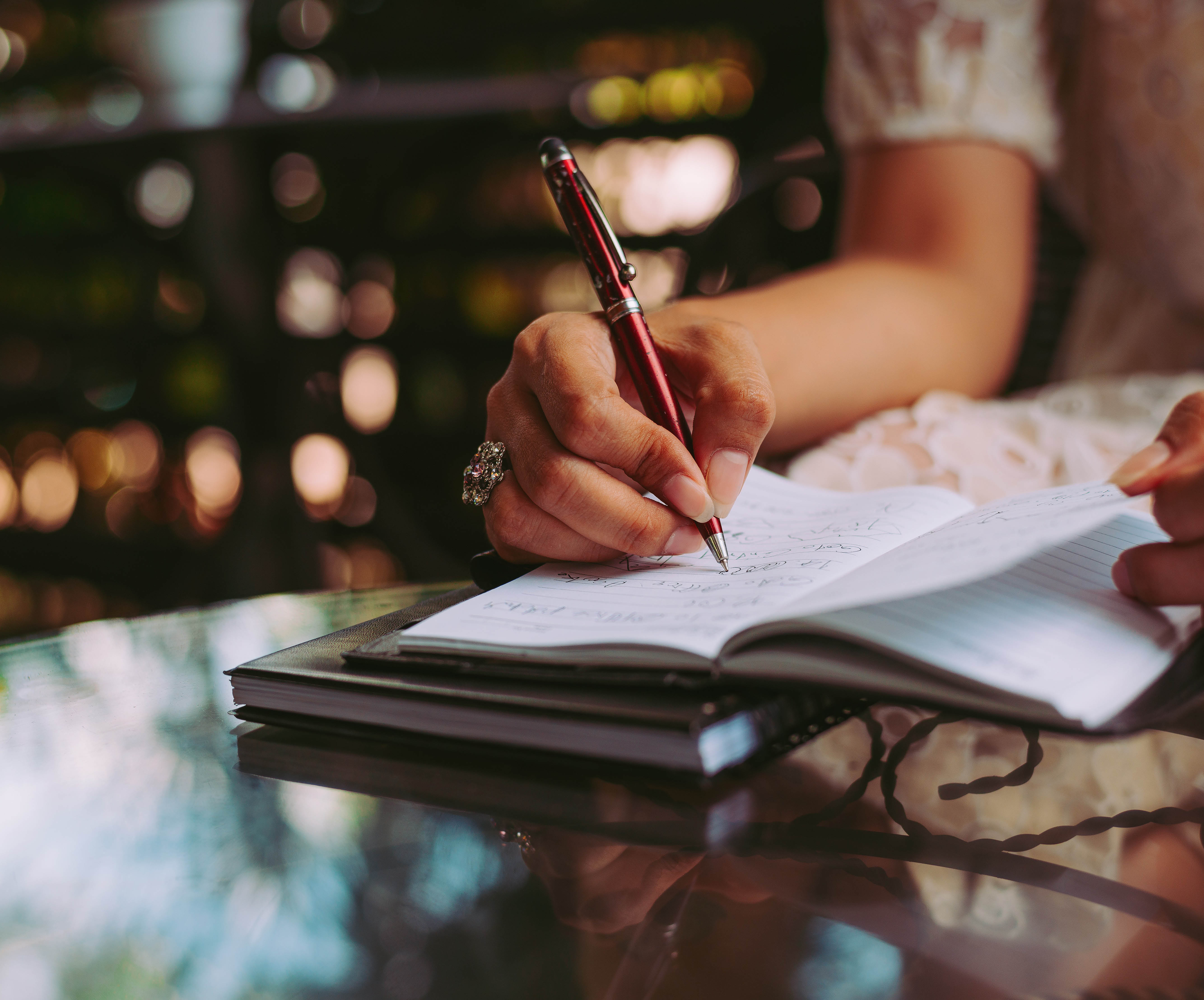 woman writing in notebook at glass table