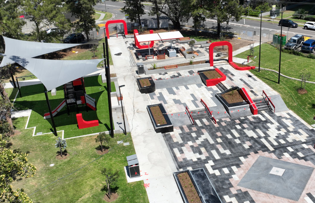Playground and shade sails next to large, paved area of skate plaza jumps