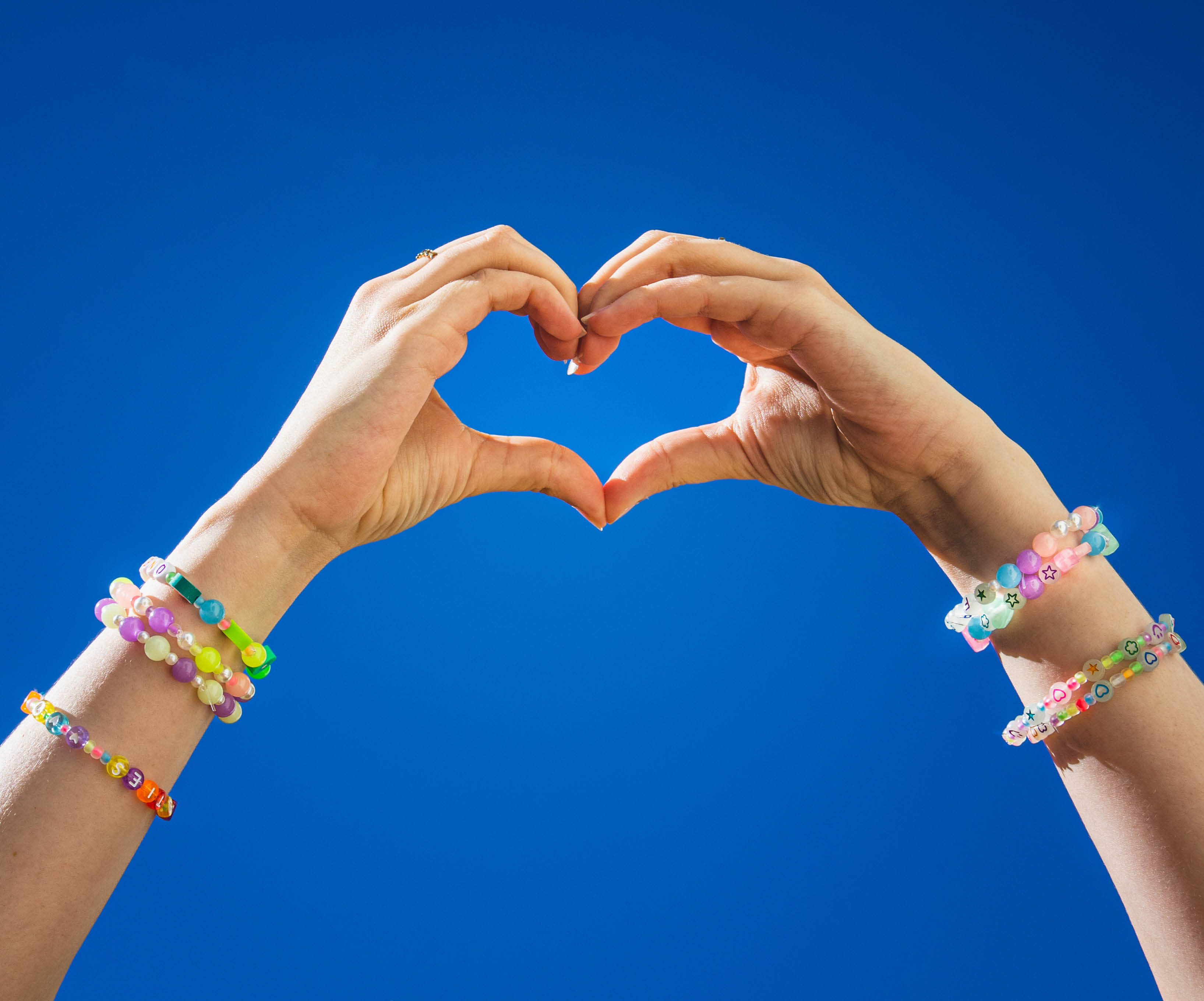 hands making hearts wearing friendship bracelets